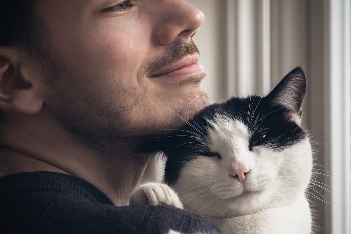 L'immagine di un uomo seduto su un divano con un gatto felice appoggiato sulle sue braccia.